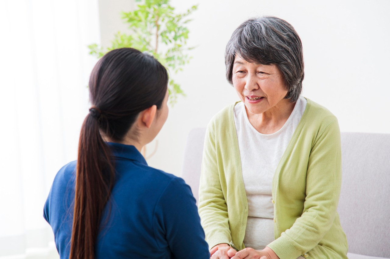 黄緑のカーディガンを着た高齢者と会話するスタッフ